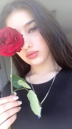 a woman holding a red rose in her right hand and looking at the camera while wearing a black shirt