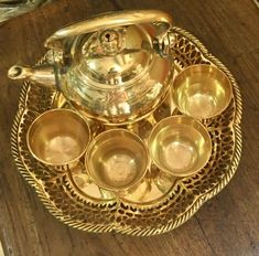 a brass tea set on a tray with cups and saucers in the middle, sitting on a wooden table