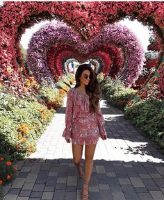 a woman walking down a walkway covered in pink and red flowers, with her hands in her pockets