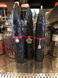 three black candles are sitting on top of a table in front of jars and containers