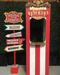 a red and white ticket booth sitting next to a green wall with signs on it