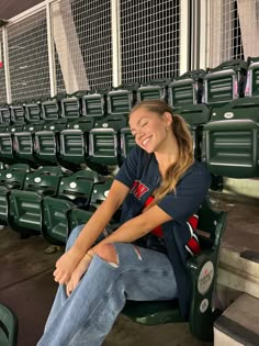 a woman sitting on top of a green bench next to a row of empty seats