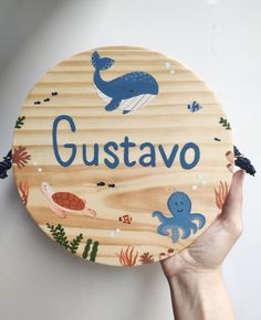 a person holding up a wooden sign that says gustavo with an octopus and whale on it