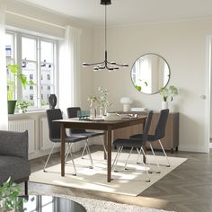 a dining room table with chairs and a round mirror on the wall above it in front of a window