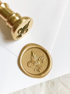 a wax stamp with a flower on it next to a white envelope and gold seal