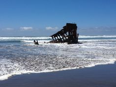 an old rusted ship sitting in the water on a beach next to the ocean