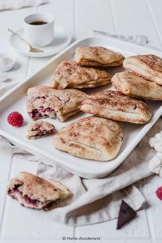 there are several pastries on the plate with raspberries next to it and a cup of coffee