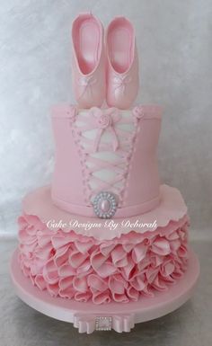 a pink cake with shoes on top and ruffles around the bottom, sitting on a table