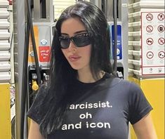 a woman with sunglasses is standing in front of a gas pump and pointing to the side