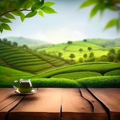 a wooden table topped with a cup of green tea next to a lush green hillside