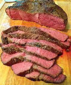 some meat is sitting on a cutting board next to another piece of meat that has been cut in half