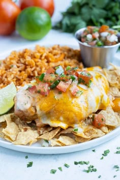 an enchilada on a plate with rice, salsa, and tortilla chips