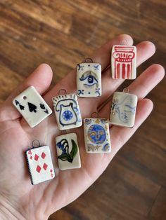 a person is holding seven miniature ceramic charms in their hand, all with different designs on them