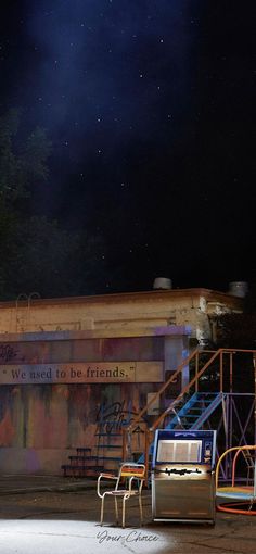 two chairs and a bench in front of a building with graffiti on the walls at night