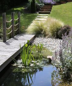 a wooden bridge over a small pond with water plants and flowers in the foreground