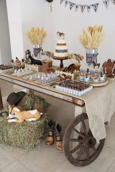 a table topped with lots of desserts next to a wooden wagon filled with hay