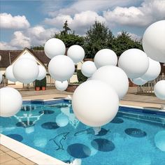 some white balloons floating in the air over a swimming pool