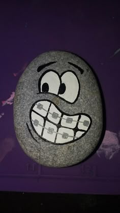 a rock with a face drawn on it sitting in front of a purple wall,