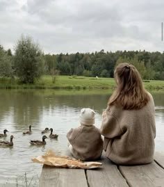 a woman and child sitting on a dock watching ducks