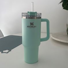 a green travel mug sitting on top of a white table next to a potted plant