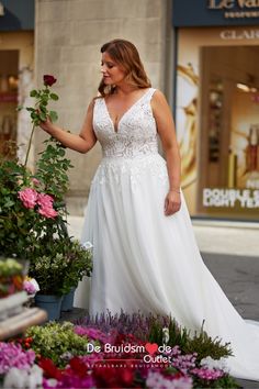 a woman in a white dress is standing next to some flowers and holding a rose