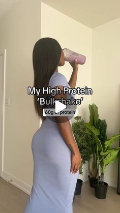 a woman in a blue dress drinking from a pink bottle with the words, my high protein bull shaker