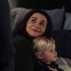 a woman sitting next to a little boy on top of a bed in front of pillows