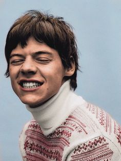 a young man with his eyes closed wearing a sweater and smiling at the camera while standing in front of a blue background