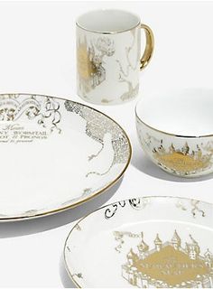 three white and gold plates, two cups and one saucer with an image of a castle on them