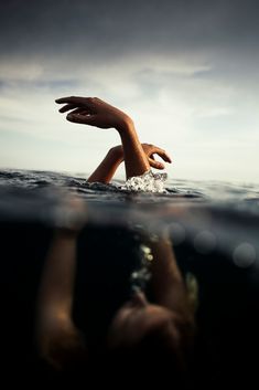 someone is swimming in the water with their hand up to the camera, and there are only two hands above the water