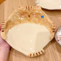 a person holding a cat shaped plate on top of a wooden table next to a bowl