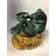 a green frog statue sitting on top of a gold leafy base with a candle in it's mouth