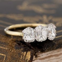 three stone diamond ring sitting on top of an old book with gold trimmings