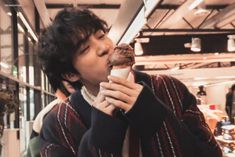 a young man eating a donut while standing in front of a store display window