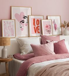 a bedroom with pink walls and pictures on the wall above the bed, along with pillows