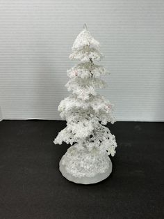 a small white christmas tree on a black surface with snow flakes all over it