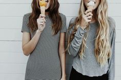 two young women eating ice cream and munching on an orange slice while standing next to each other