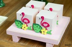 three small boxes with flamingos on them are sitting on a wooden table next to some flowers