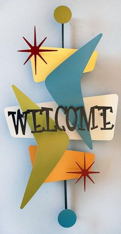 a welcome sign hanging from the side of a wall next to a blue vase with red, yellow and green stars on it