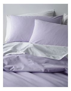 an unmade bed with purple sheets and white pillow cases on top of each other