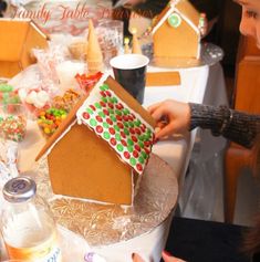 a woman decorating a gingerbread house with candy and candies on the table