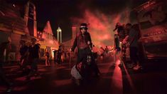 a group of people walking down a street at night with fireworks in the sky behind them