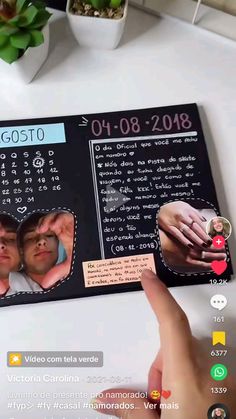 a hand pointing at a photo on a table next to a potted plant and cell phone