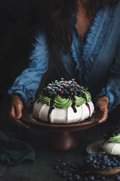 a woman is decorating a cake with green and white frosting on it, surrounded by berries