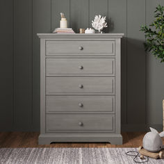 a grey chest of drawers sitting on top of a wooden floor next to a potted plant