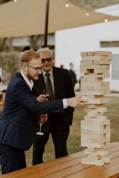 a man in a suit and glasses playing with a wooden block tower on a table