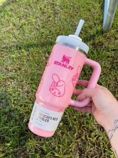 a person holding a pink cup in their hand on the grass with an animal drawn on it