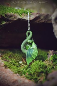 a green dragon necklace hanging from a chain with moss growing on it's side