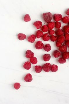 raspberries are scattered on a white surface