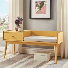 a yellow bench sitting in front of a window next to a vase with flowers on it